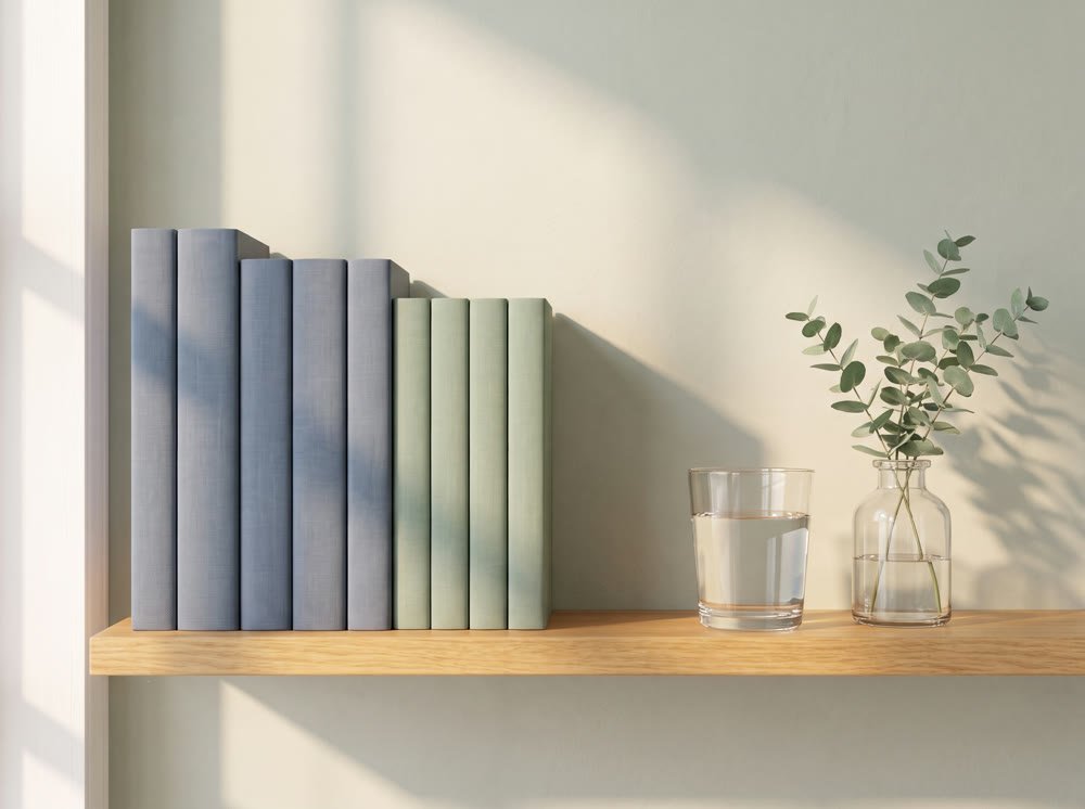 A sunlit oak shelf of sage and slate blue guides beside a glass of water and a sprig of eucalyptus