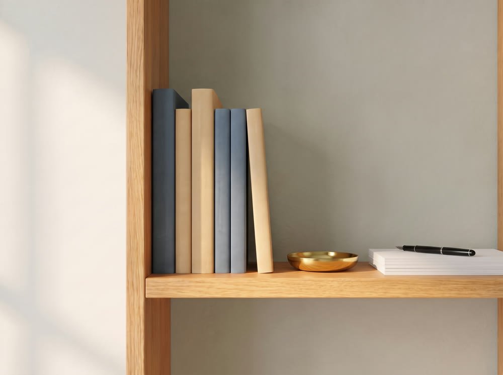 A sunlit oak shelf of slate and wheat colored guides beside a small brass dish and a fountain pen